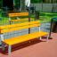 Ryga Bench w/ Backrest, sárga fa pad szürke fém vázzal kültéri játszótéren.