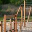 Trim trail fa mászó- és egyensúlyozó elem játszótéri homokos talajon, zöld háttérrel.