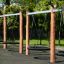 Double Swing Robinia (BNS 120) fából készült hinta fekete ülőkékkel játszótéren, zöld környezettel