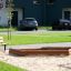 5-angle palisade sandbox fa kerettel, homokozó egy parkban, mellette pad található.
